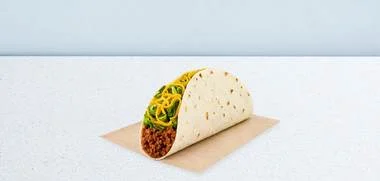 Soft-shell taco filled with seasoned ground beef, shredded lettuce, and cheese on a napkin.
