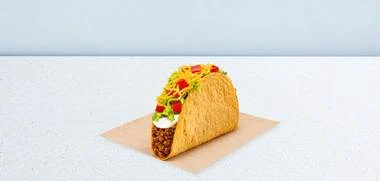 A beef taco filled with lettuce, cheese, and salsa on a paper liner on a pale blue surface.