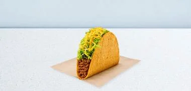 Single hard-shell taco filled with ground meat, shredded lettuce, and cheese on a parchment square.